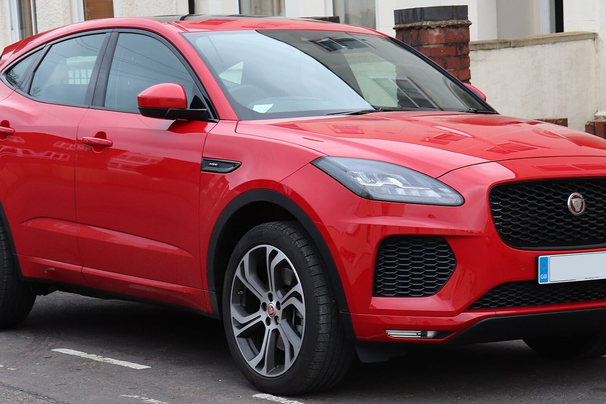 A red Jaguar E-Pace compact SUV with grey alloy wheels parked at a curb in front of a white house