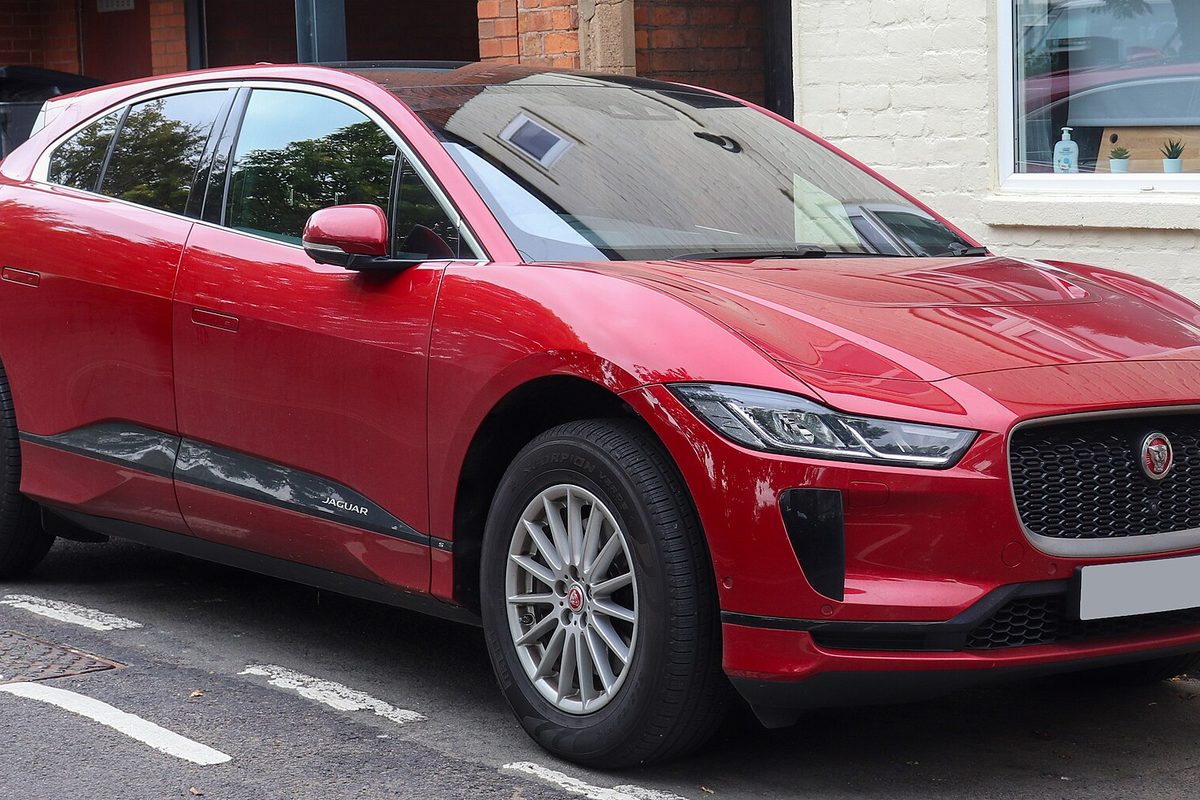 A red Jaguar I-Pace electric crossover parked at a curb in front of a brick building