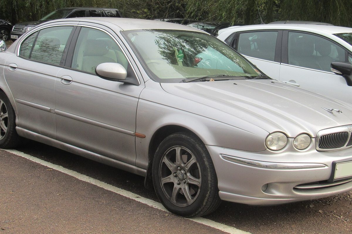 A silver Jaguar X-Type sedan parked at a curb under trees, seen from the front three-quarter