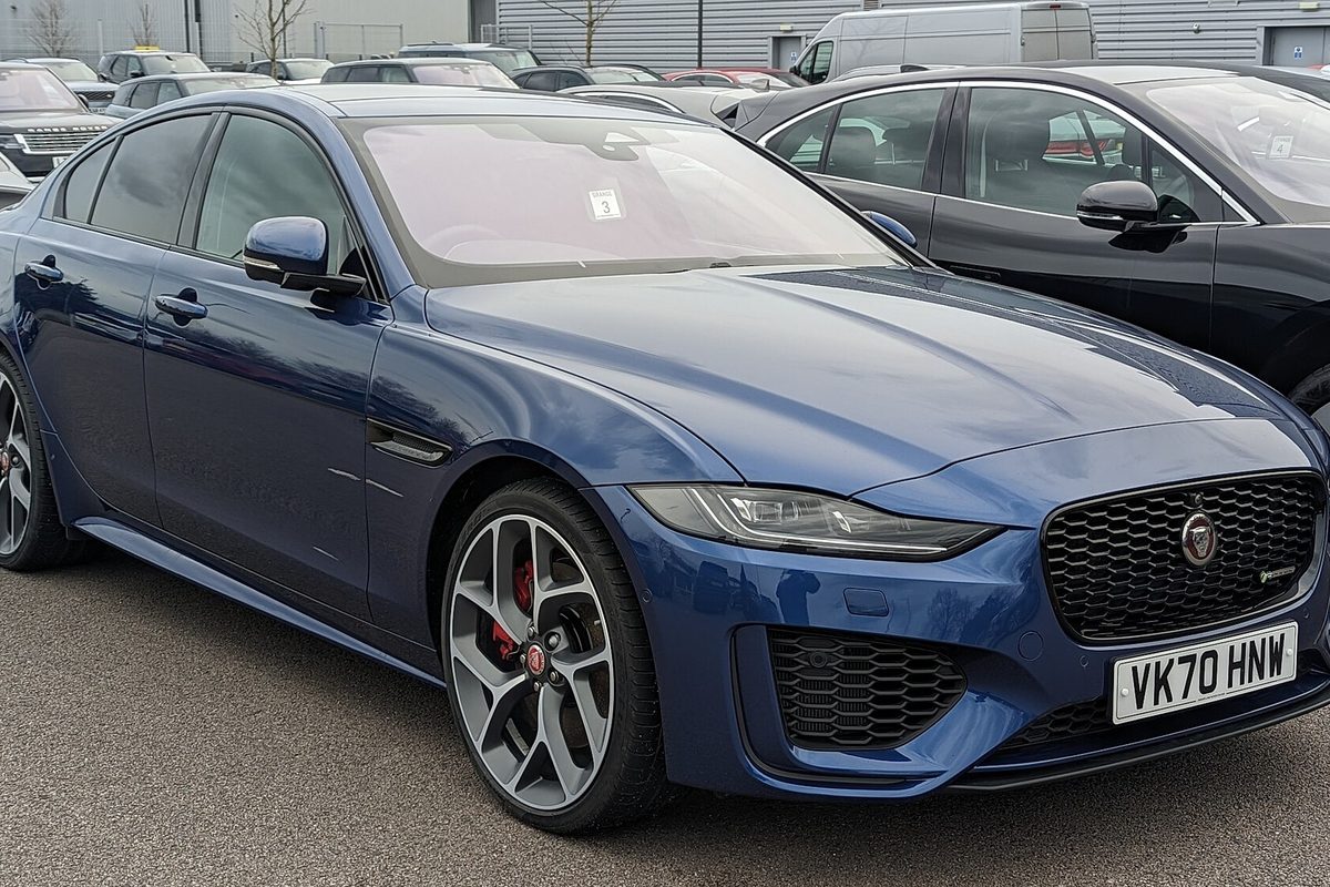 A dark blue Jaguar XE sedan with black mesh grille and red brake calipers, parked in a lot among other cars