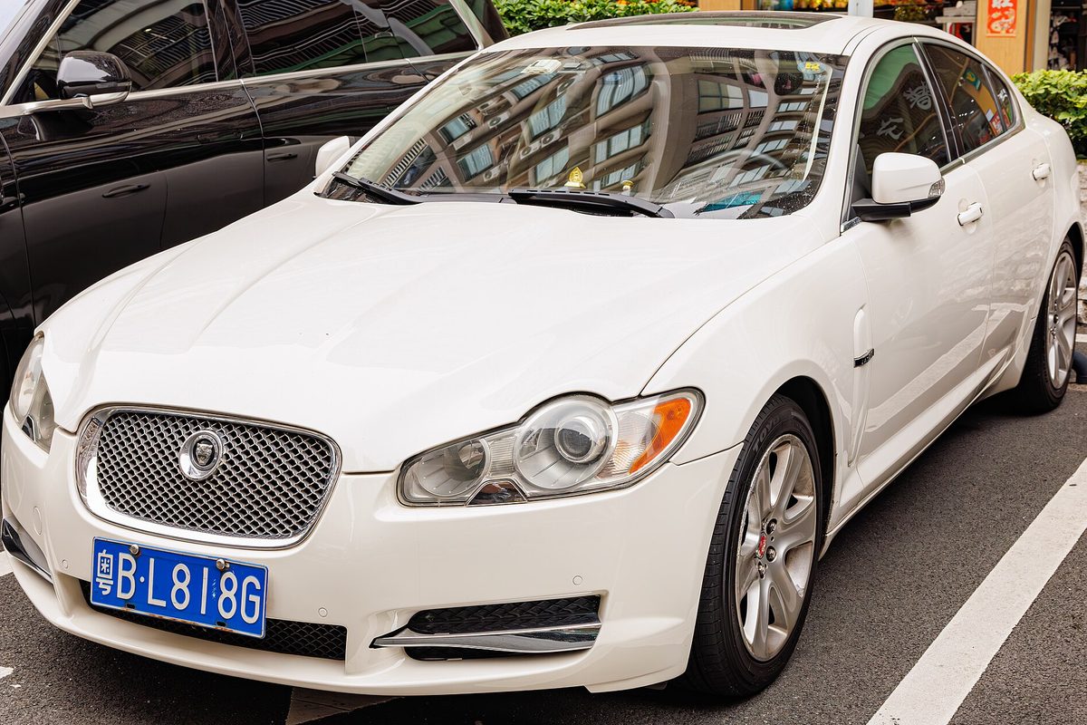 A white Jaguar XF sedan with a chrome mesh grille, parked in a marked city parking space between other cars