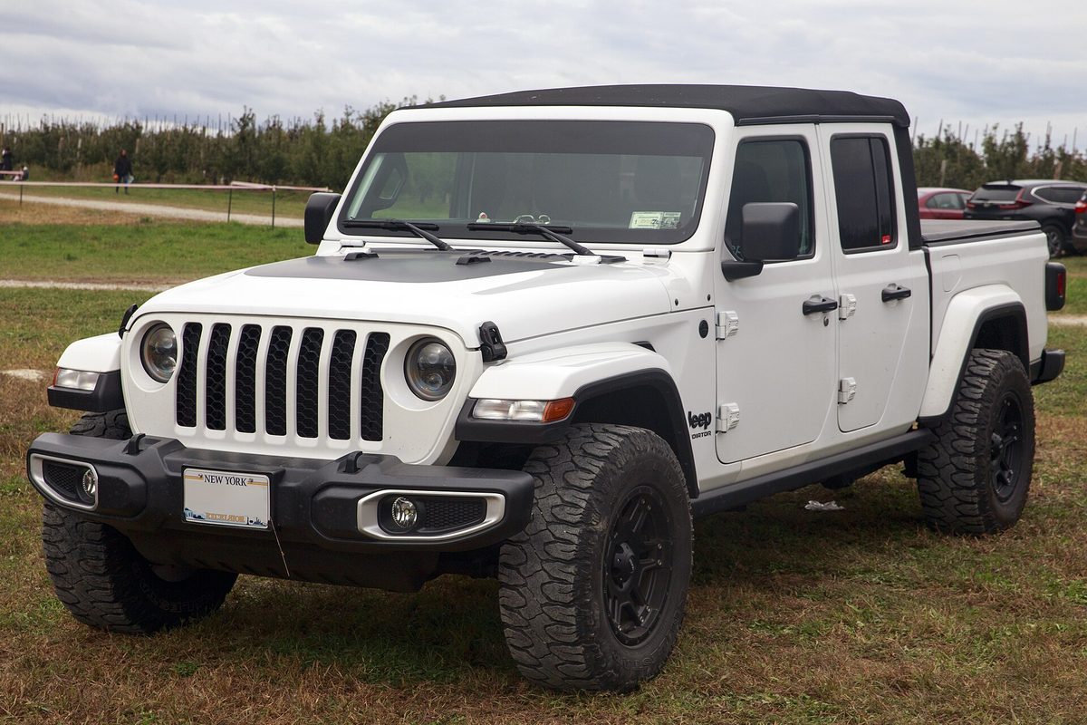 A white 2021 Jeep Gladiator Sport crew-cab pickup with a black soft top and black wheels, parked on grass