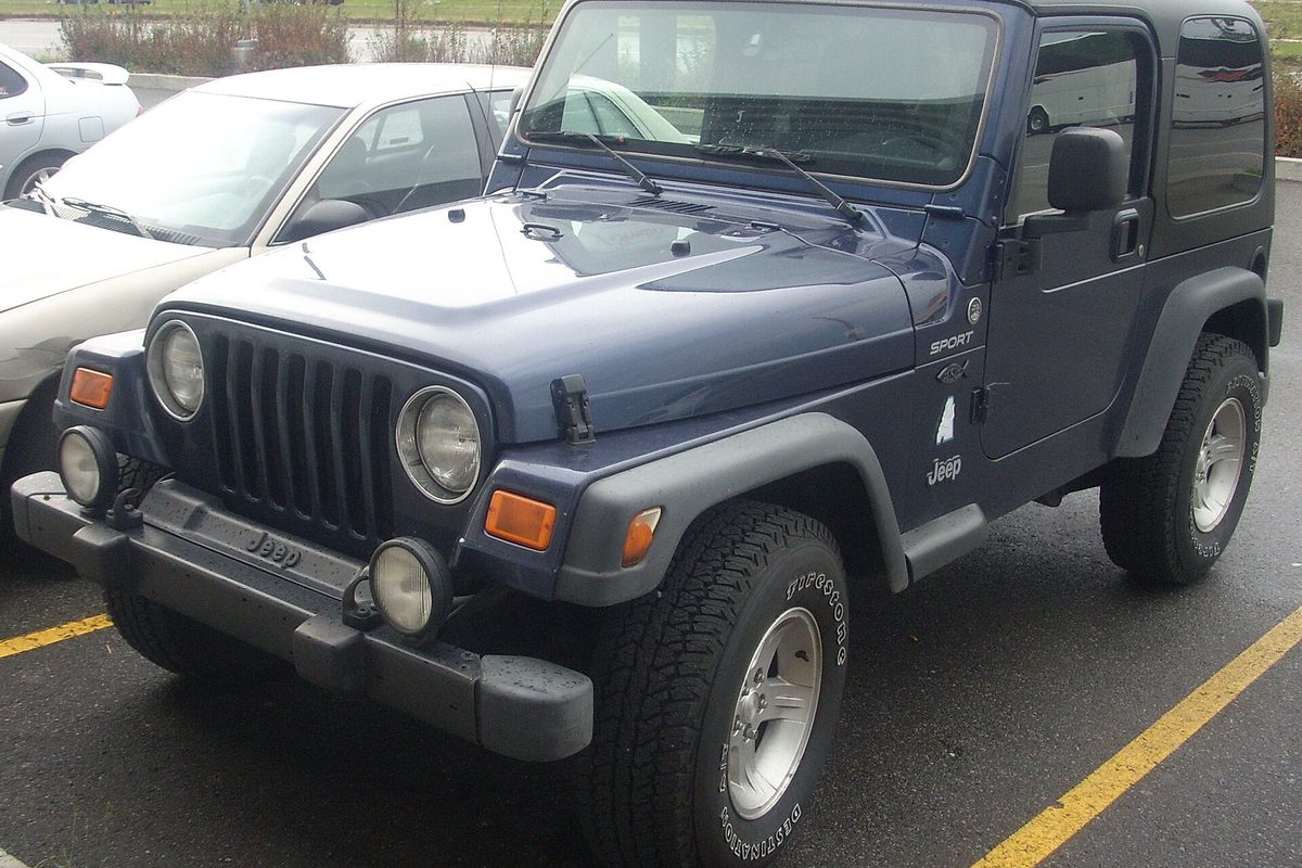 A dark blue two-door Jeep Wrangler TJ Sport with a hardtop, round headlights and gray fender flares, parked across yellow lot lines