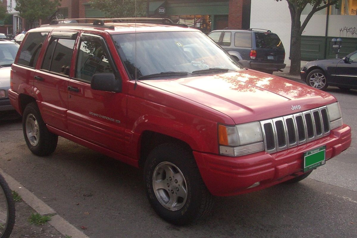 A red 1990s Jeep Grand Cherokee parked at the edge of a lot