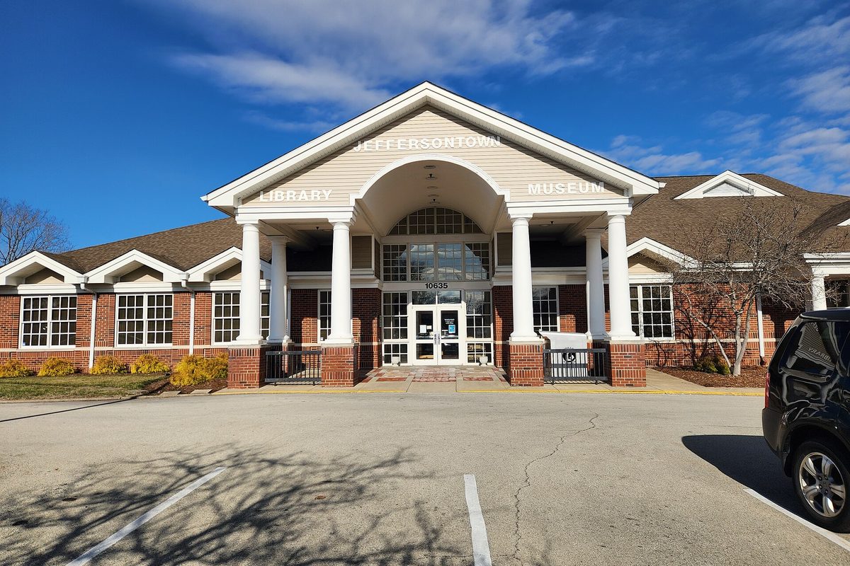 The white-columned entrance of the Jeffersontown Library and Museum under a deep blue sky, with an empty parking lot in front