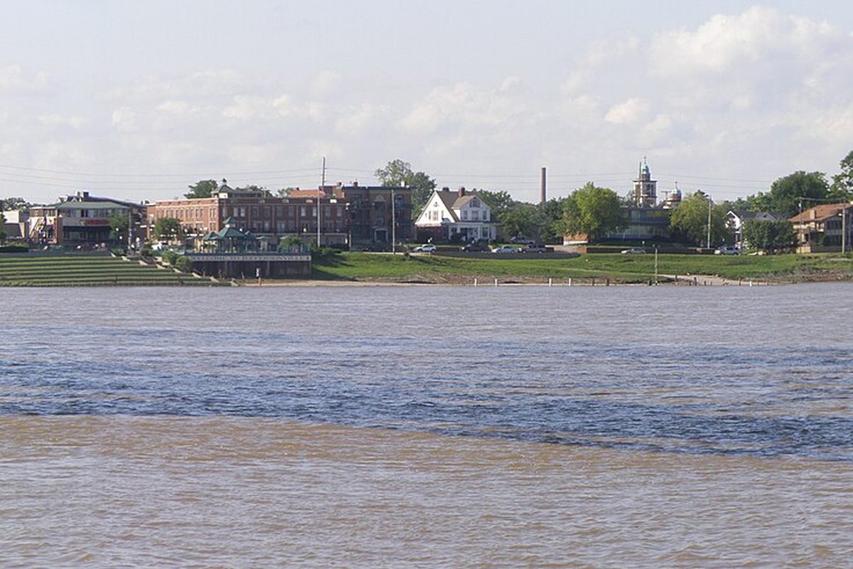 Jeffersonville's riverfront seen from the Ohio River, with brick buildings, a gazebo and a grassy bank above brown water