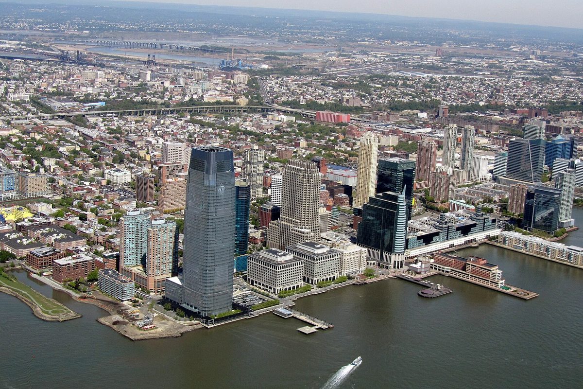 Aerial view of the Jersey City waterfront, its glass towers along the river and rowhouse blocks stretching inland