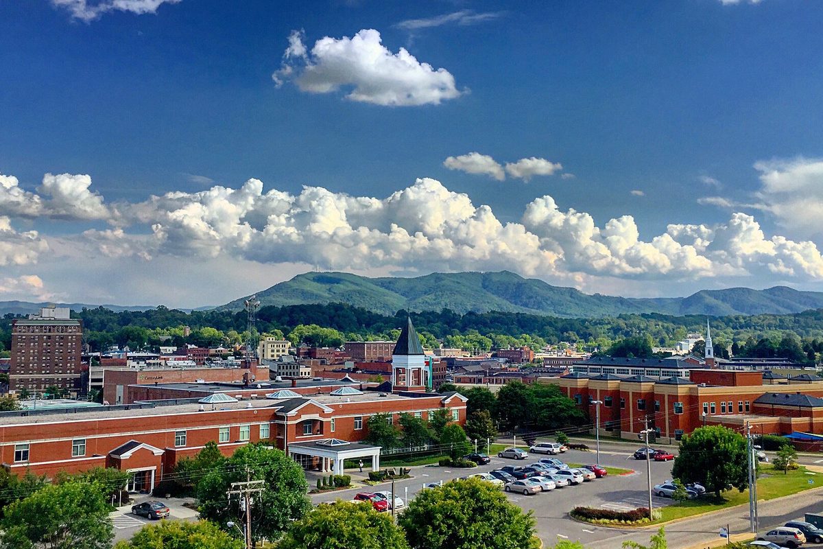 Downtown Johnson City's red-brick buildings and a white steeple under summer clouds, with Buffalo Mountain rising behind
