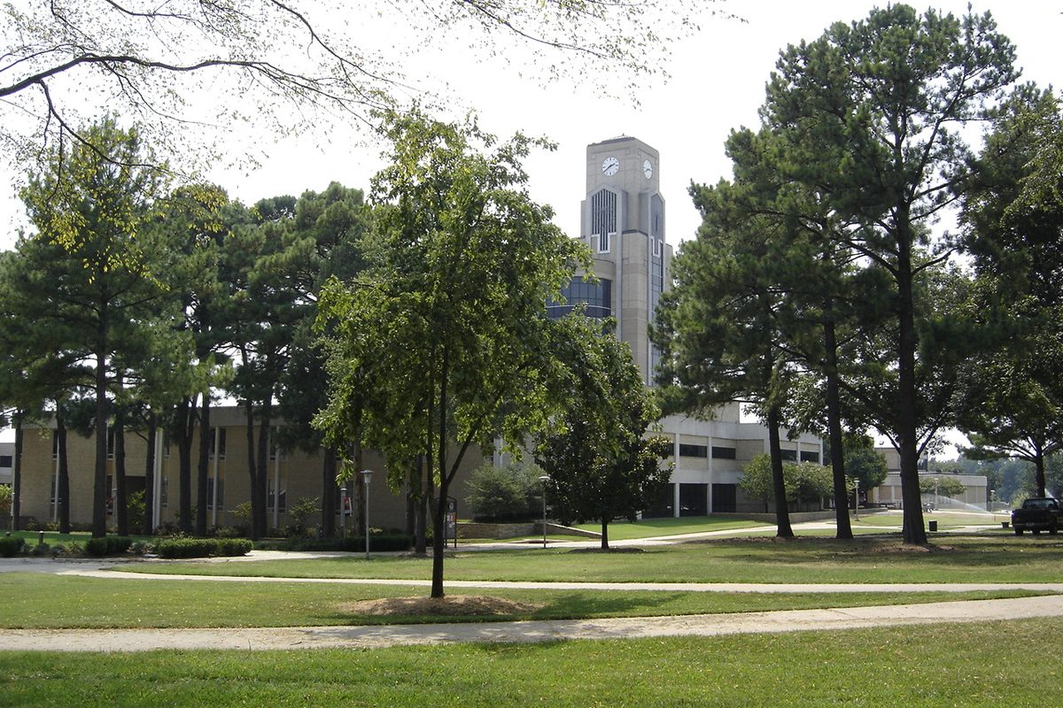 The clock tower of Arkansas State University's Dean B. Ellis Library in Jonesboro, behind tall pine trees and a wide green lawn