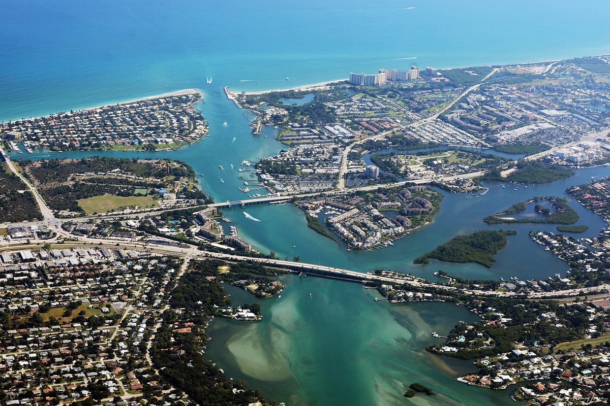 Aerial view of Jupiter Inlet, where the Loxahatchee River meets the Atlantic, with two bridges, marinas, homes and a sandy shoal in turquoise water