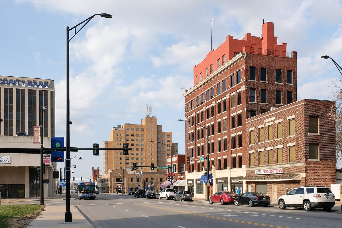 North 7th Street in downtown Kansas City, Kansas, with a red brick tower building, a tan high-rise, a city bus and cars on the street