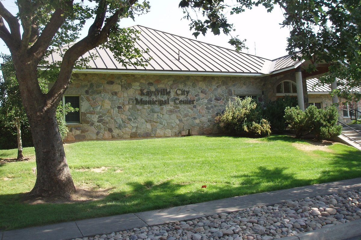 The stone-walled Kaysville City Municipal Center with a green metal roof, a large shade tree and a lawn in front
