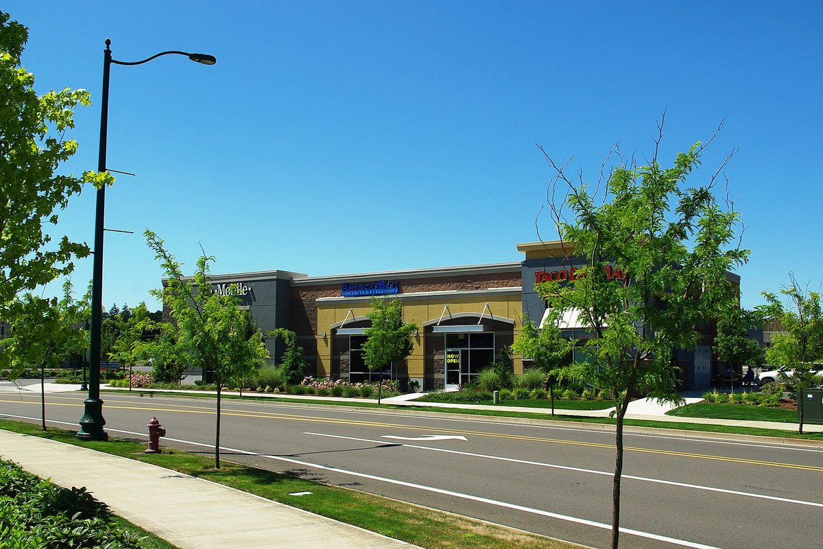 A tan and brick shopping center building at Keizer Station behind a young street tree and a red fire hydrant under a blue sky