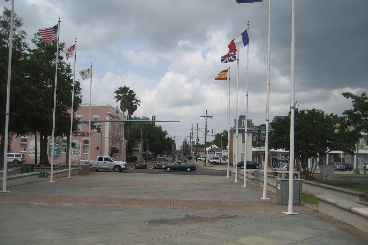 A row of flagpoles flying the U.S., French, British and Spanish flags over a brick plaza in Kenner's Rivertown, looking up Williams Boulevard