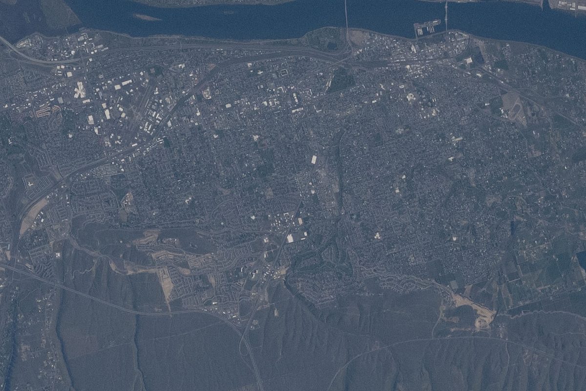Space station photo of Kennewick's street grid and neighborhoods, with the Columbia River along the top edge and open hills below