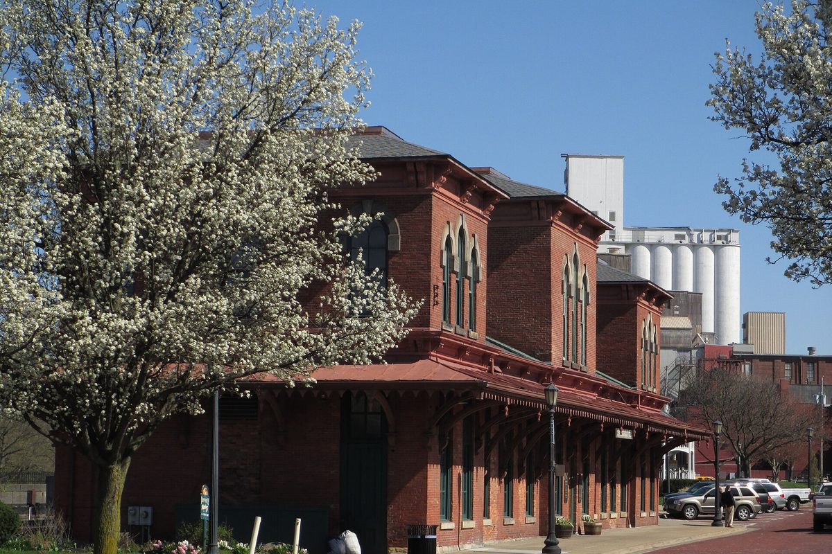 Kent's red brick 1875 Atlantic & Great Western railroad depot beside white-blossomed trees, with the Star of the West grain silos rising behind it