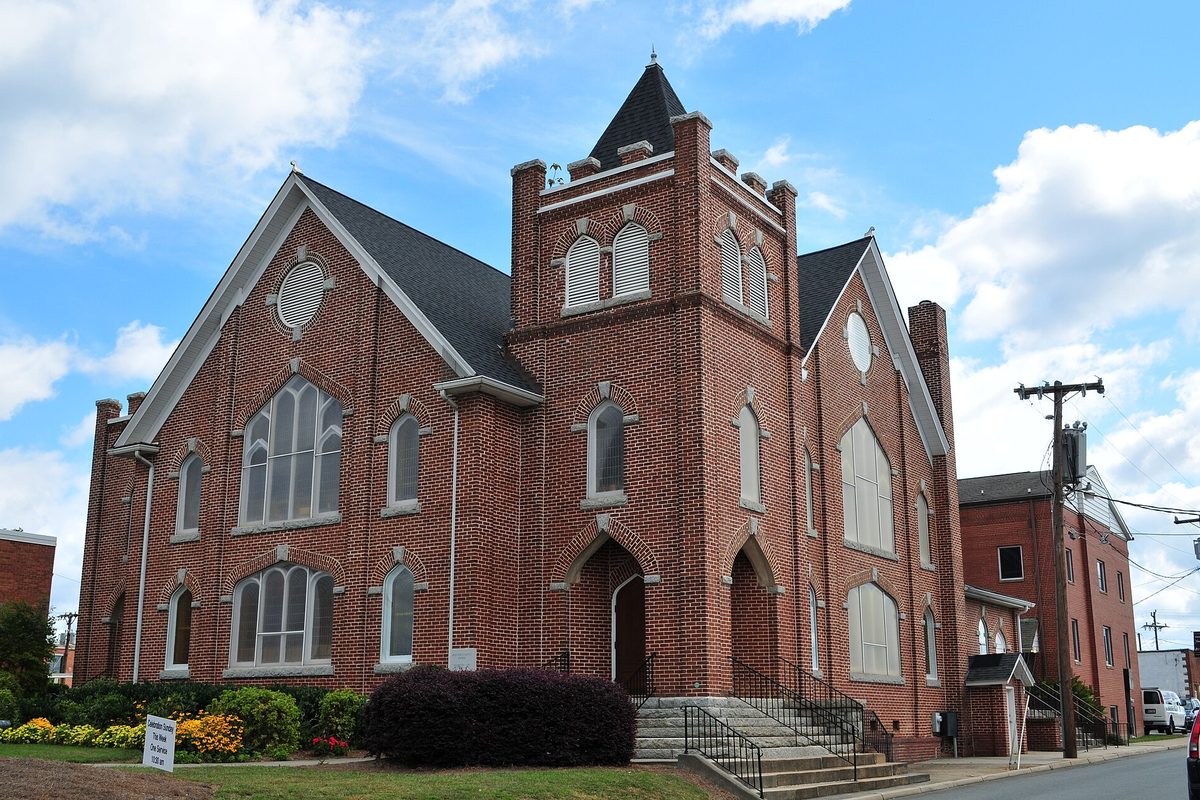 The red brick First Baptist Church on North Main Street in Kernersville, with arched windows, a square bell tower and flower beds by the front steps