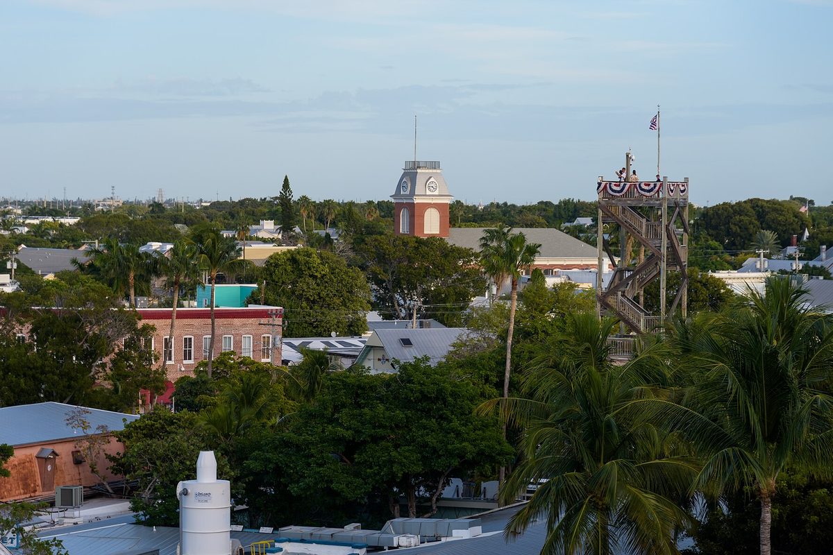 Key West rooftops looking east, with a red-brick clock tower, palm trees and a tall wooden lookout tower draped in flag bunting