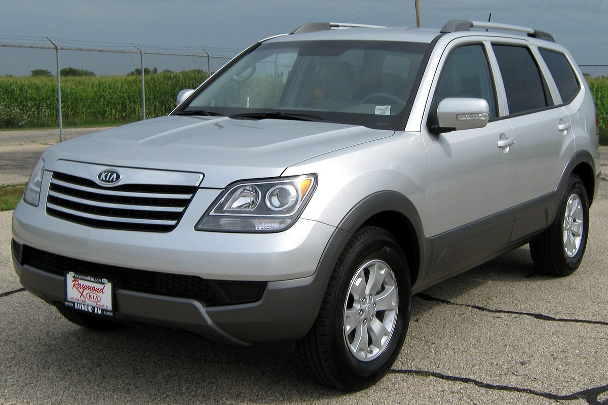 A silver 2009 Kia Borrego SUV on a dealer lot beside a cornfield, seen from the front left
