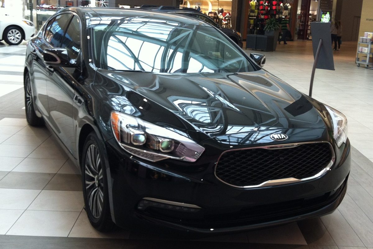 A black 2015 Kia K900 sedan on display inside a shopping mall, seen from the front right