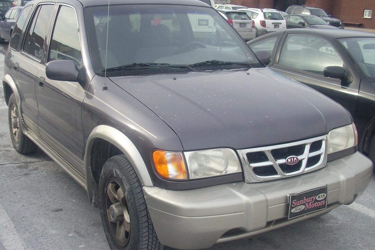 A dark gray 2002 Kia Sportage four-door with tan lower body panels and a chrome grille, parked in a dealer lot