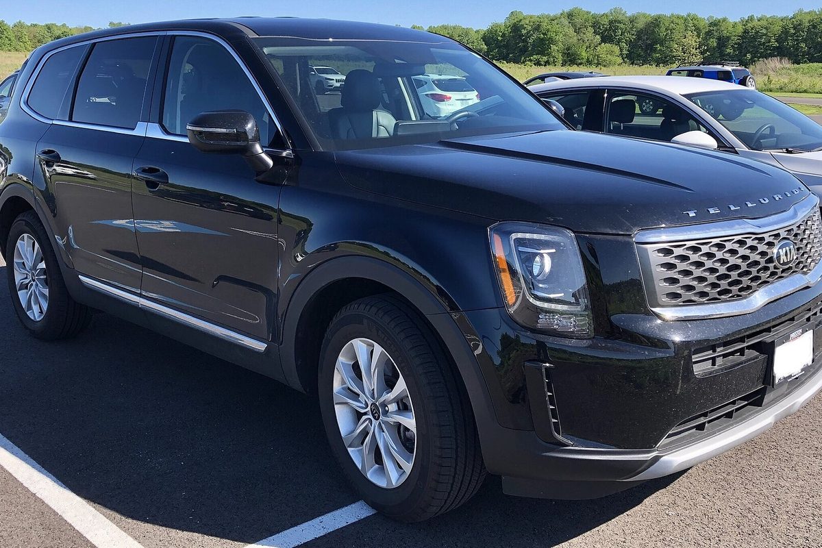 A black first-generation Kia Telluride SUV parked in a sunny lot, seen from the front corner, with a silver car behind it