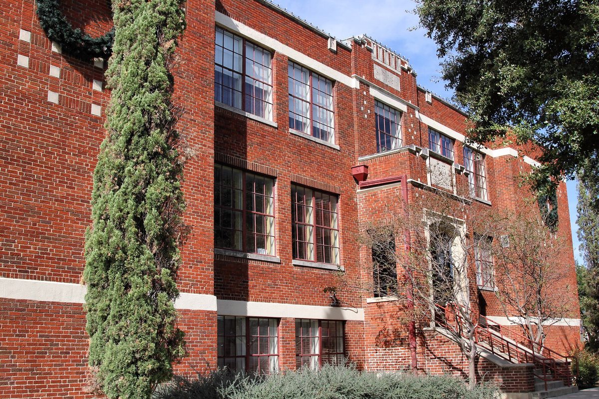 The red brick former Avenue D School, now Killeen City Hall, with tall paned windows, a front stair and a narrow evergreen tree by the wall