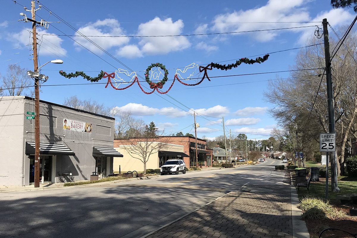 A quiet street in historic downtown Knightdale with a bakery storefront, a 25 mph speed limit sign and a holiday garland strung over the road