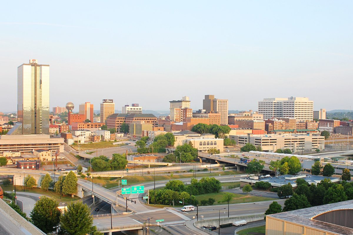 Downtown Knoxville skyline with a tall gold glass tower and the gold Sunsphere rising above highway interchanges and green trees