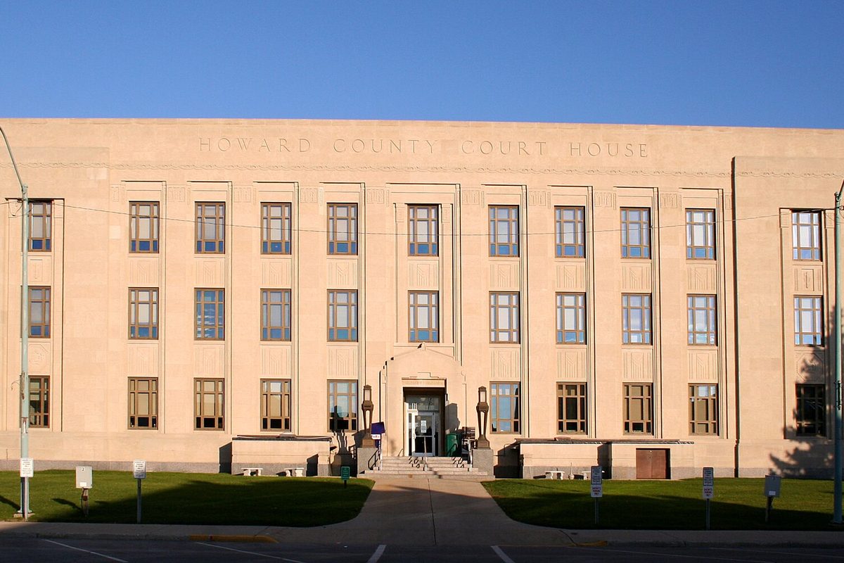 The pale stone Howard County Court House in Kokomo, its name carved above rows of tall windows, in evening light