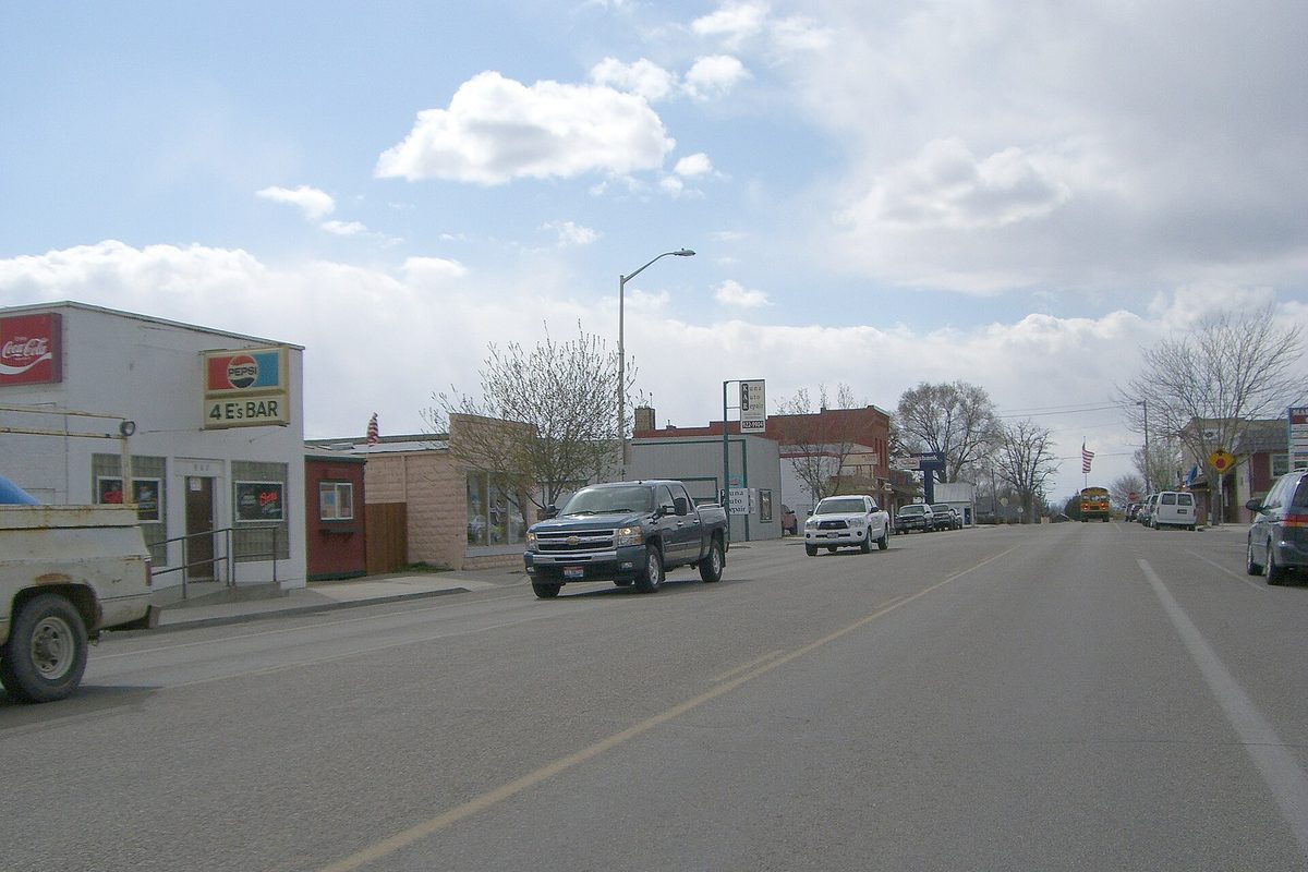 Main Street in Kuna, with pickup trucks driving past low storefronts under a partly cloudy sky