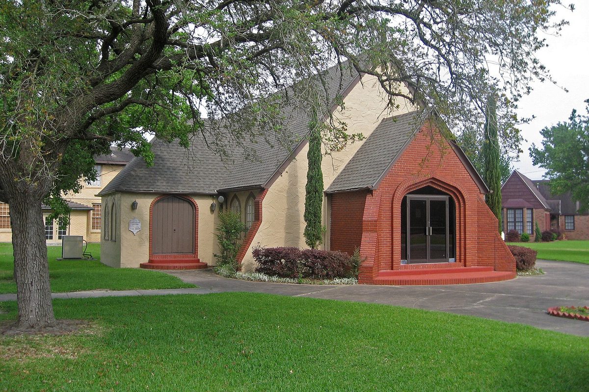 Paul's Union Church in La Marque, a small church of cream stucco and red brick with arched doorways, beneath a spreading oak on a green lawn