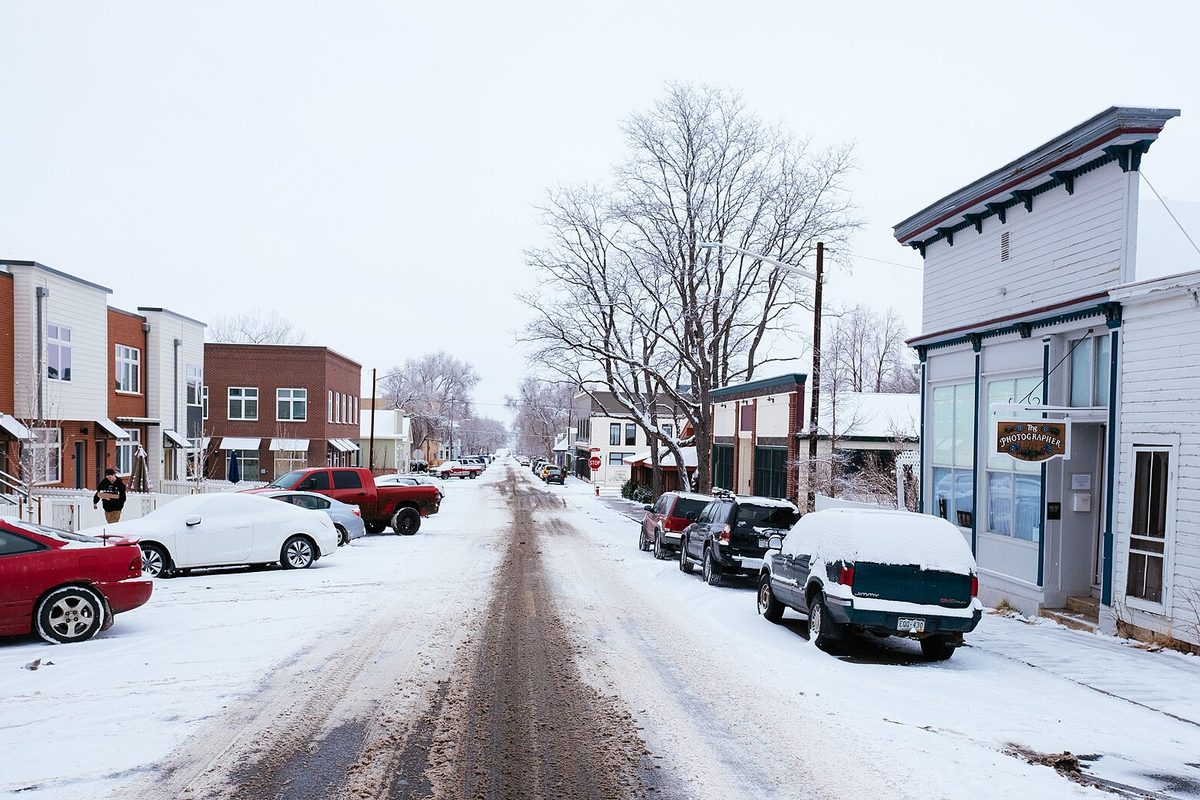 Snow-covered East Simpson Street in Lafayette, with cars parked along both curbs, bare trees and small storefronts
