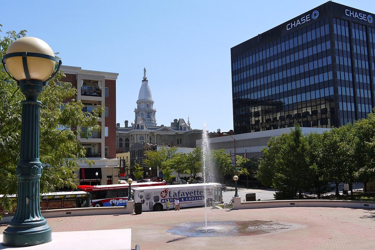 Riehle Plaza in downtown Lafayette, with a fountain, a globe lamp post and a CityBus, and the Tippecanoe County Courthouse dome behind