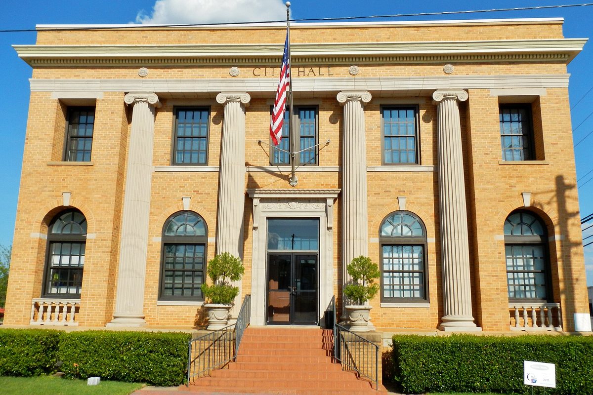 LaGrange City Hall, a two-story yellow brick building with tall white columns, arched windows, CITY HALL lettered above the entrance, an American flag and red brick steps