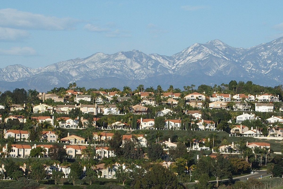 Rows of red-tile-roofed tract homes on a Laguna Niguel hillside, with the snow-capped Santa Ana Mountains behind them