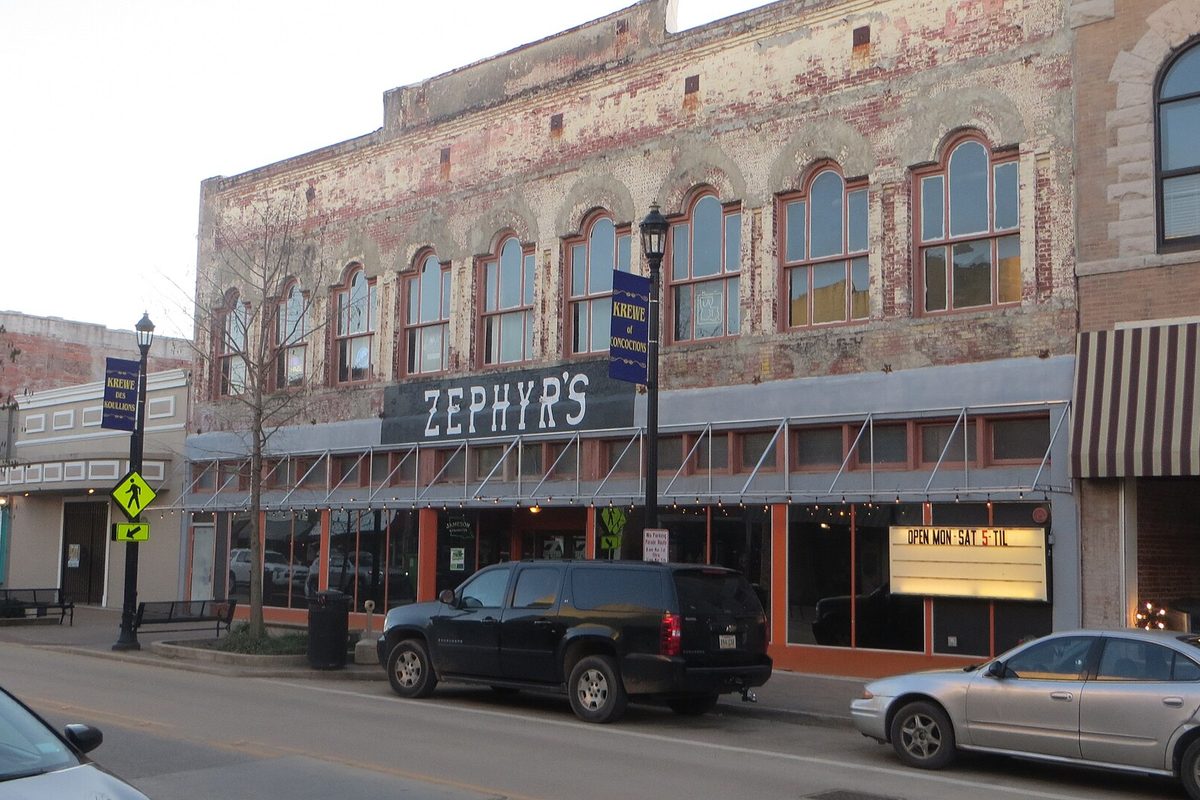 The arched-window brick front of Zephyr's on a downtown Lake Charles street, with an SUV and a sedan parked out front