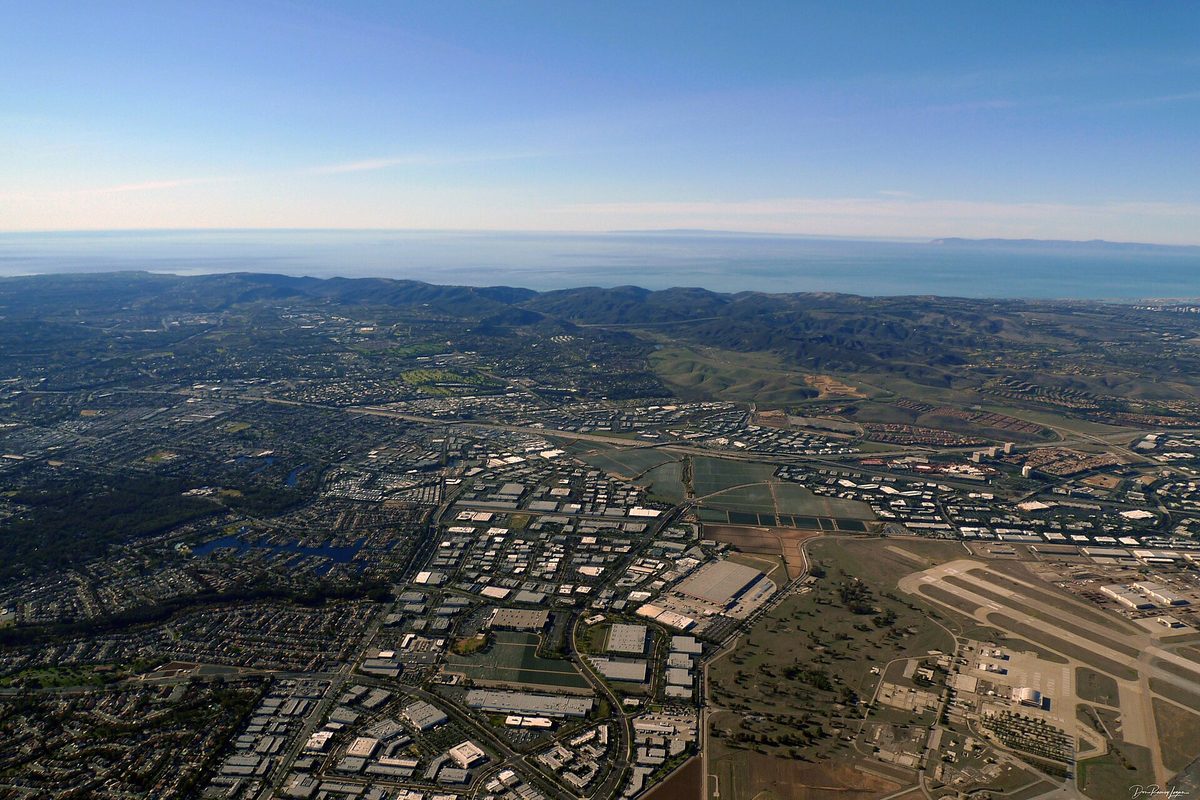 Aerial view over Lake Forest and Laguna Hills, business parks and neighborhoods spreading toward green hills and the Pacific Ocean