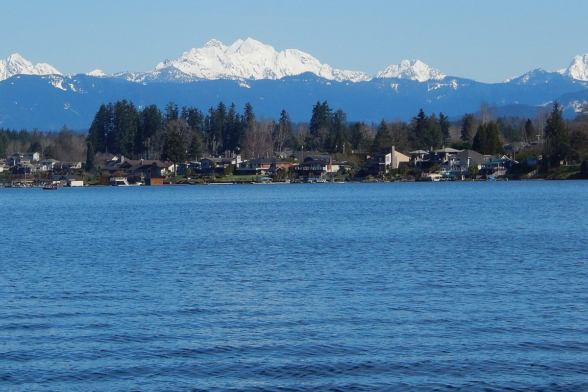 Blue water of Lake Stevens with houses and evergreens along the far shore and snow-covered Cascade peaks rising behind them
