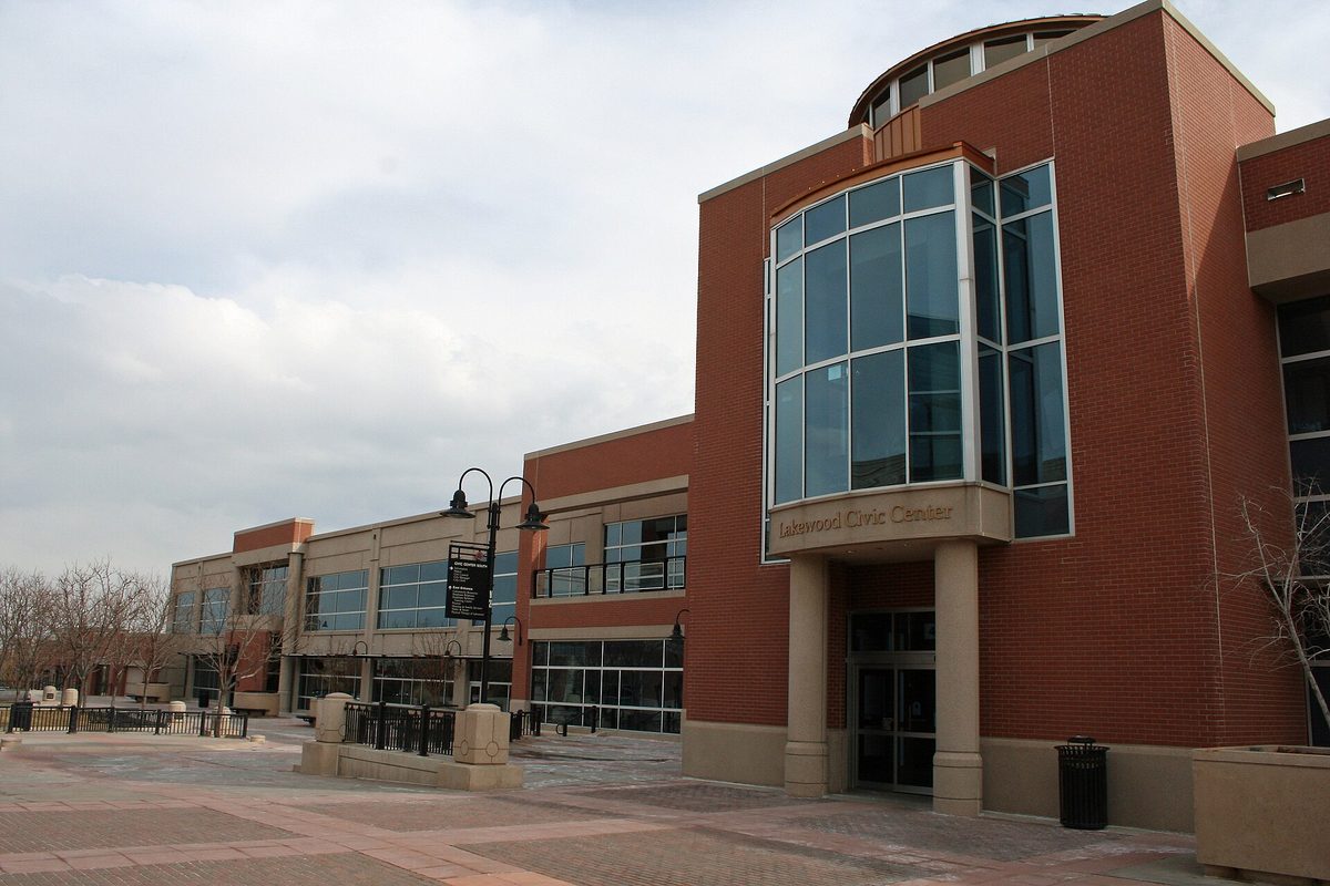 The red brick Lakewood Civic Center with a round glass tower over its entrance, seen across a paved plaza under a cloudy sky