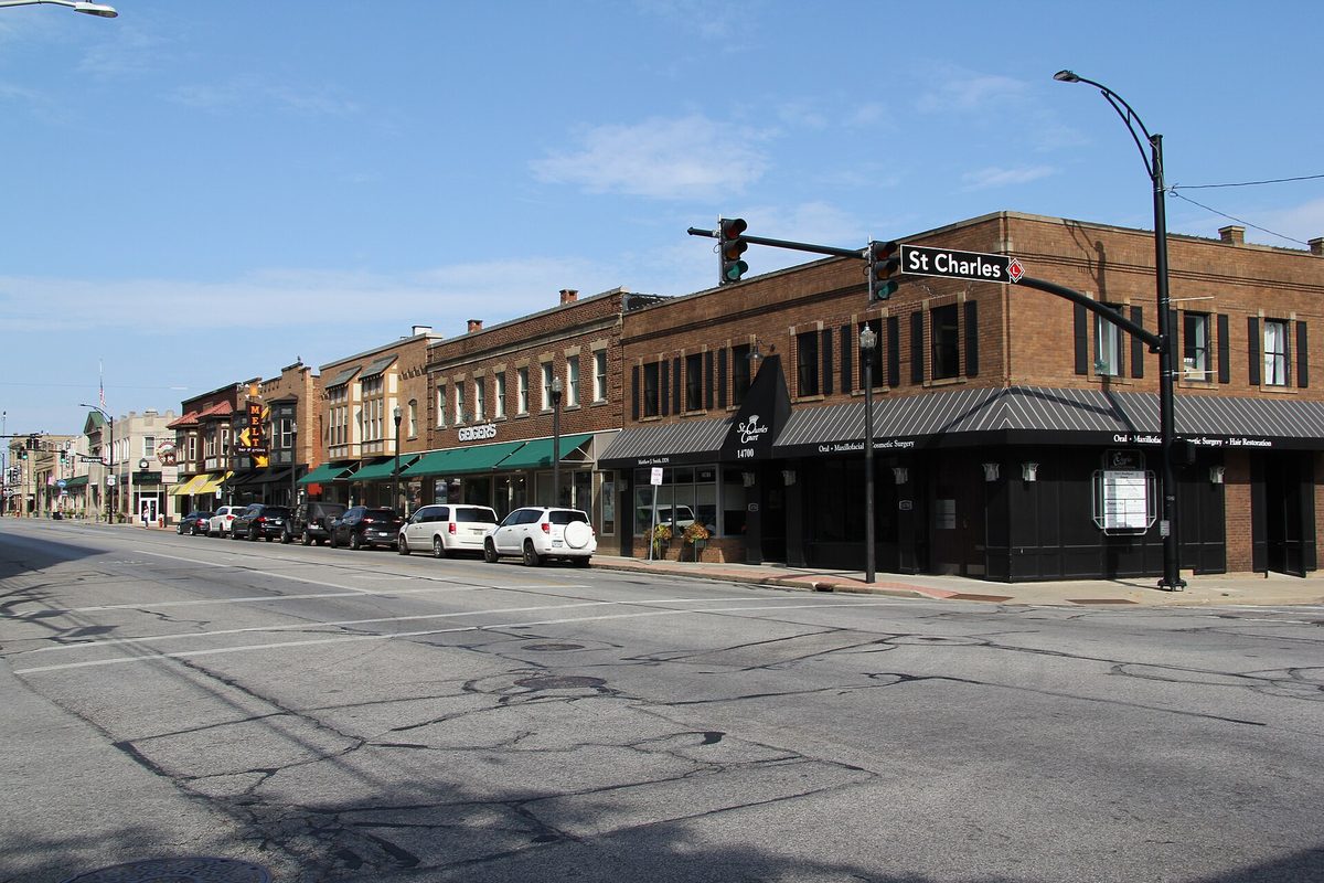 Two- and three-story brick storefronts with green awnings along a main street in Lakewood's downtown historic district, at the St. Charles street sign