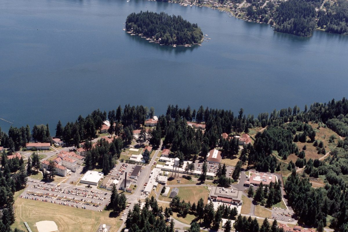 Aerial view of the VA Puget Sound American Lake campus on the wooded shore of American Lake, with a small tree-covered island in the water
