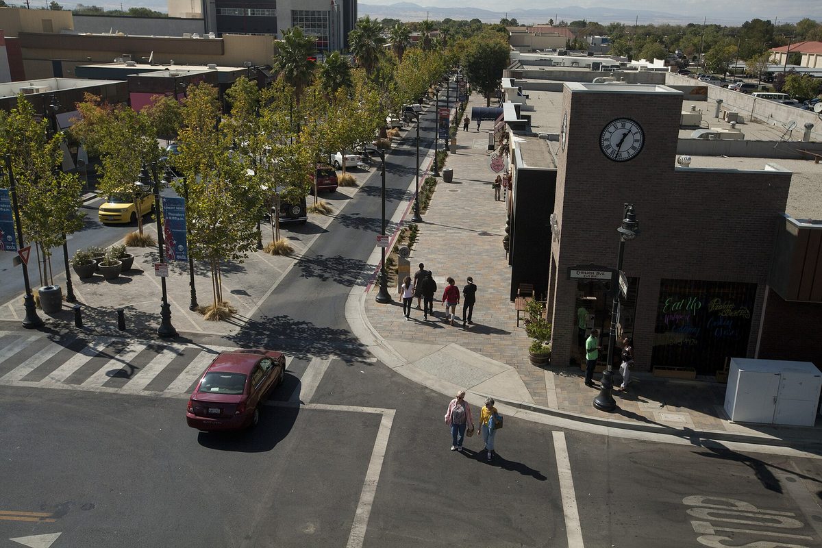 Lancaster Boulevard downtown seen from above, with a clock tower on a corner building, tree-lined sidewalks, pedestrians and a red car at the crosswalk