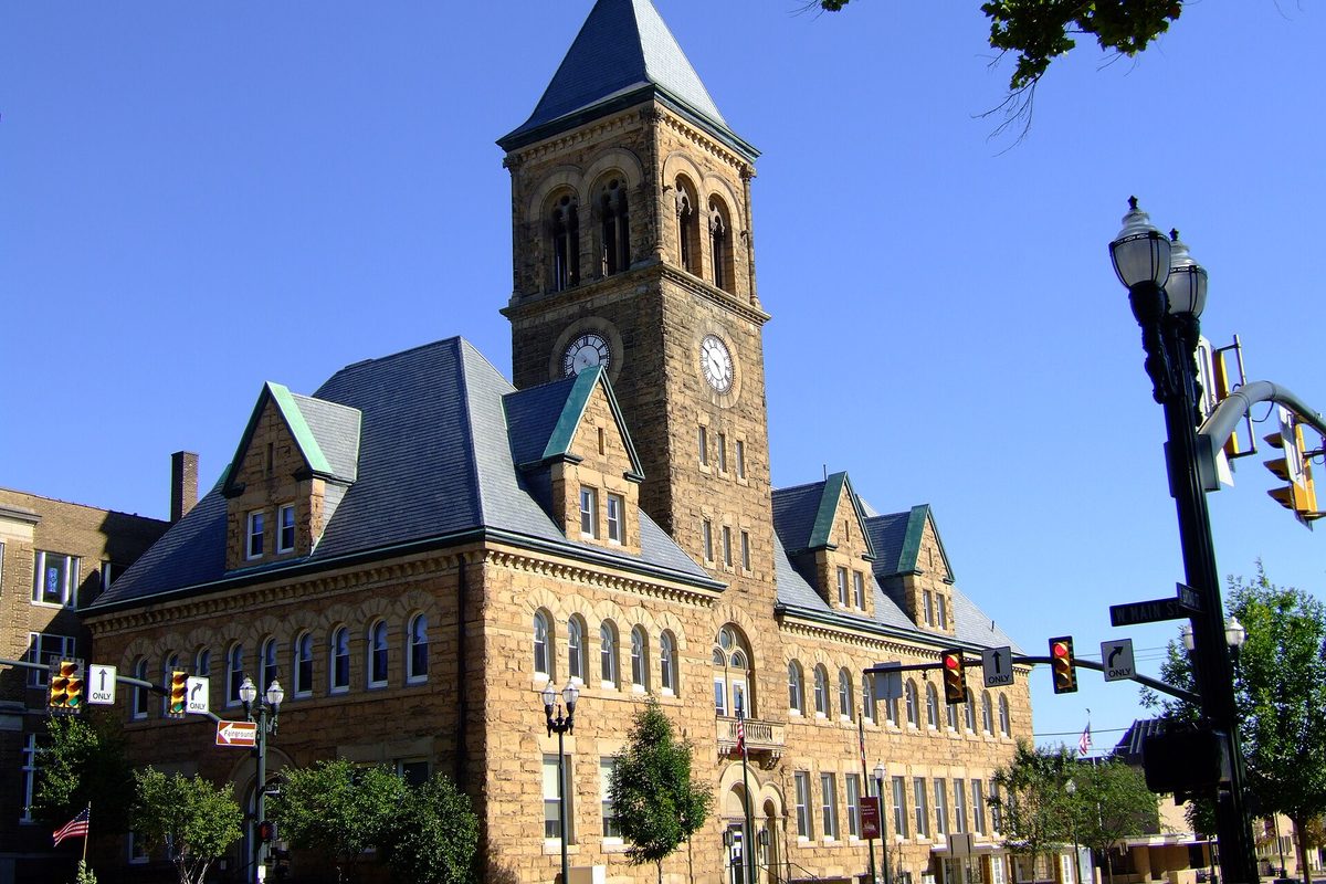 Lancaster's Romanesque stone town hall with a square clock tower and slate roof, on a sunny downtown corner with traffic lights