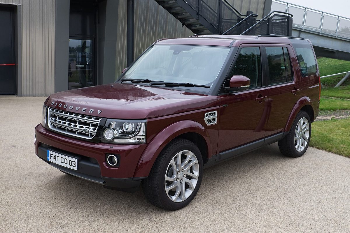 A dark red 2016 Land Rover Discovery 4 HSE parked on concrete in front of a metal-clad building with an outdoor steel staircase