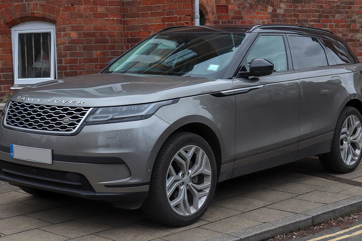 A grey 2018 Range Rover Velar HSE parked on a paved pavement in front of a red brick building with a white-framed window