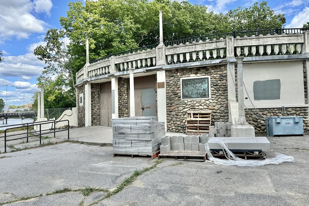 The stone and concrete front of the J. H. Moores Memorial Natatorium in Lansing's Moores Park, with pallets of concrete blocks stacked on the pavement in front