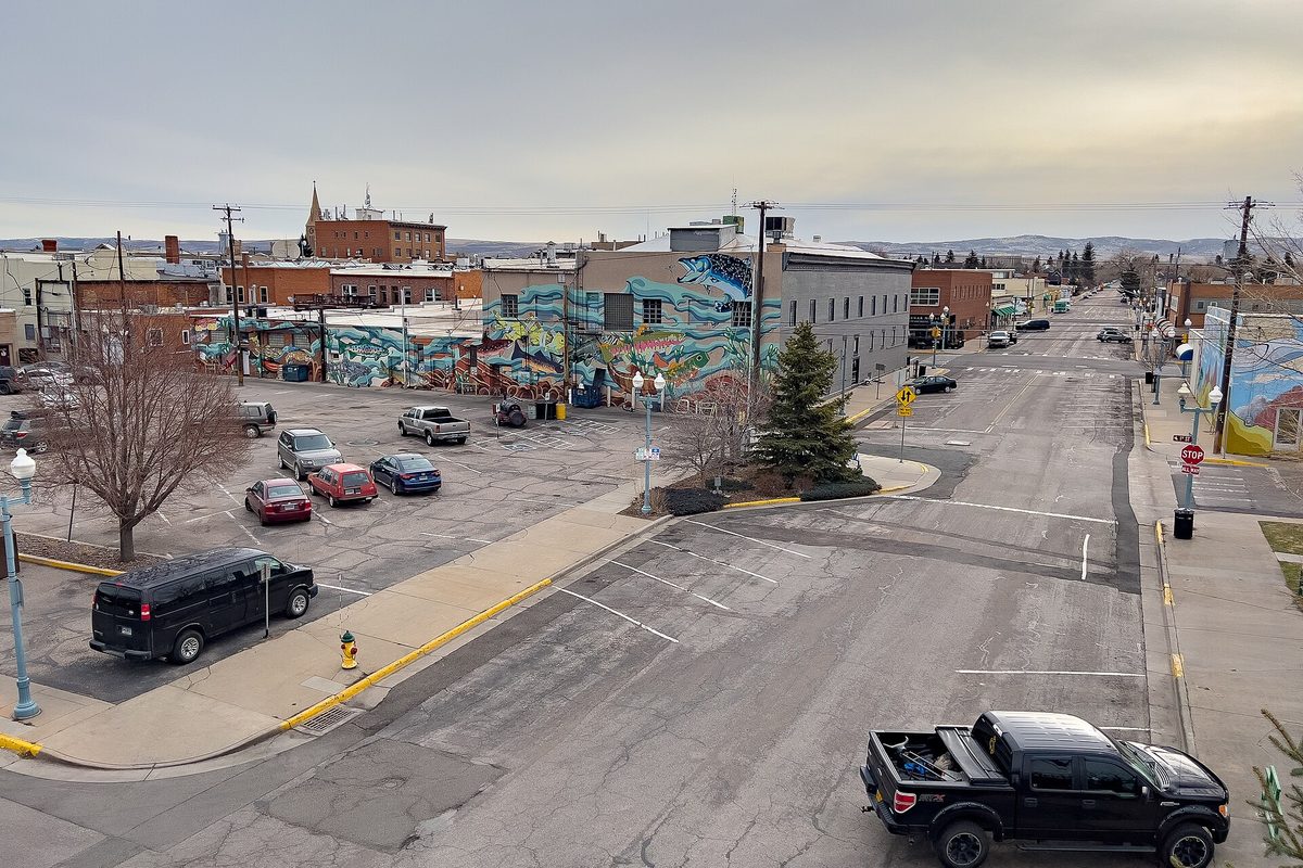 A downtown Laramie street seen from above, with a large colorful mural on a brick building, cars in a parking lot and a black pickup on the corner
