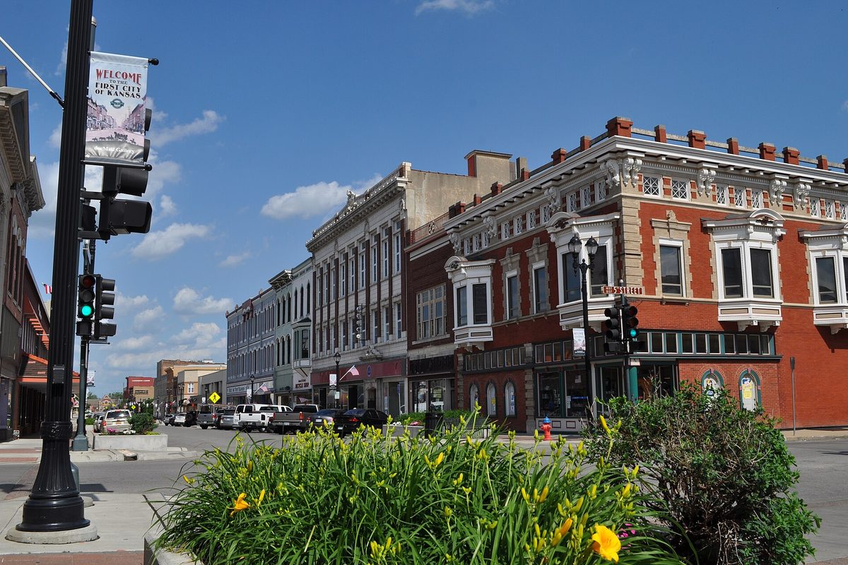 Ornate brick storefronts and a welcome banner on a light pole at Delaware and Fifth in downtown Leavenworth, with yellow lilies in front
