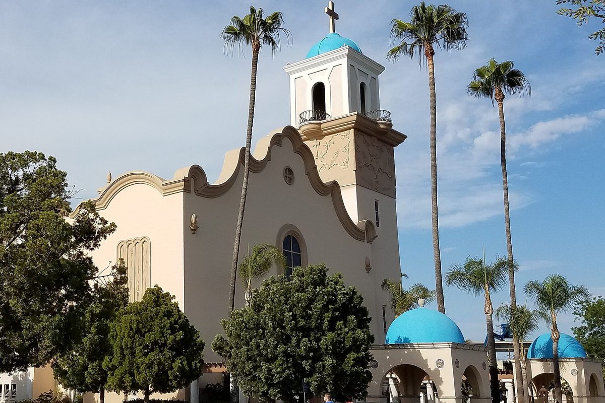 St. John of the Cross church in Lemon Grove, a cream stucco building with a bell tower and blue domes, framed by tall palm trees